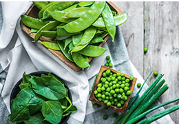 Top down shot of freshly harvested peas, pea pods, chives and spinach leaves.