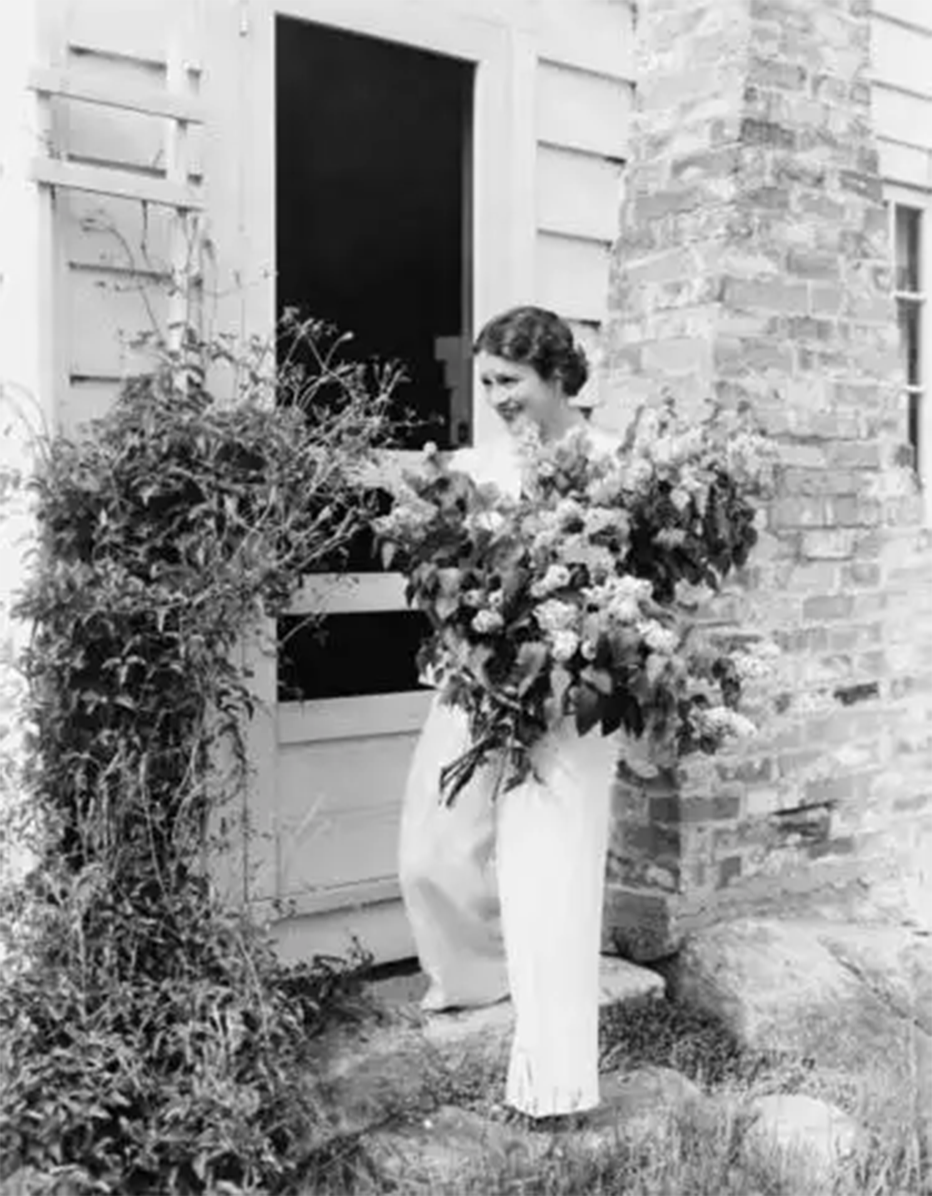 Vintage picture in black and white of a woman holding a bundle of fresh cut flowers in her arms